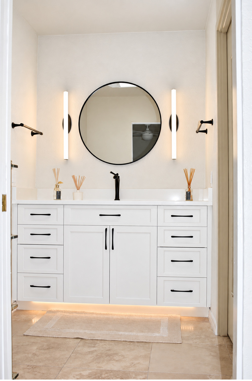 White vanity with round mirror and illuminated wall lights